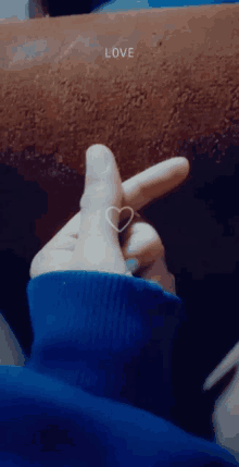 a person wearing a blue sweater is making a heart shape with their finger