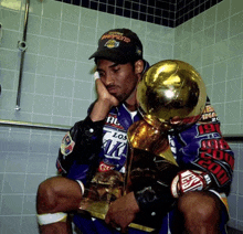 a man wearing a los angeles lakers hat sits with a trophy