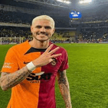 a man in a soccer jersey is standing on a soccer field giving a peace sign .