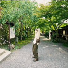 a woman wearing a mask stands on a gravel path in front of a sign that says ' a ' on it