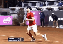 a man in a red shirt is running on a tennis court in front of a scoreboard that says taberner on it