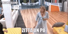 a woman in a white dress is standing in a living room with the words zitta un po ' on the floor .