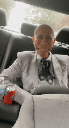 a man in a suit and tie is sitting in the back seat of a car holding a can of coke