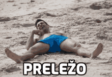 a man in blue shorts is laying on the sand with the word prelezo written above him