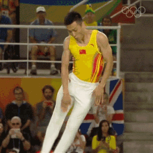 a man in a yellow tank top and white pants is doing a trick in front of a crowd at the olympics