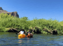 two people in kayaks on a river with a rock in the background