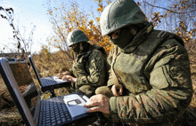 two soldiers are working on their laptops and one has a patch that says russia