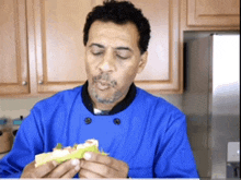 a man in a blue chef 's coat is eating a sandwich