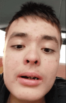 a close up of a young man 's face with a black jacket on