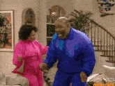 a man in a blue jacket and a woman in a pink suit are dancing in a living room