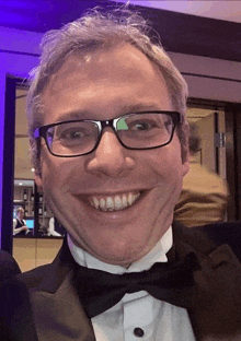 a man wearing glasses and a tuxedo is smiling for the camera