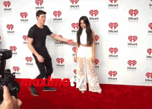 a man and woman are standing on a red carpet in front of a wall that says iheart radio on it