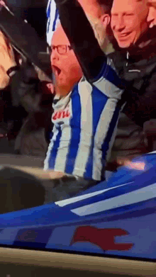 a man in a blue and white striped shirt is sitting in a stadium with his arm in the air .