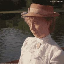 a woman wearing a straw hat and a white shirt is sitting in a boat in front of a lake