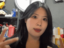 a woman giving a peace sign in front of a shelf full of cleaning supplies including a bottle of clorox