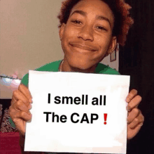 a young man holds a sign that says i smell all the cap