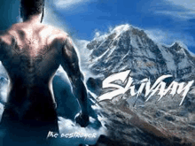 a man with a tattoo on his back is standing in front of a snow covered mountain .