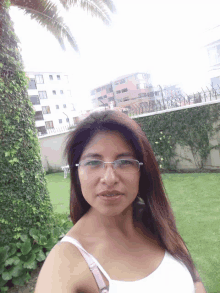 a woman wearing glasses and a white tank top stands in a garden