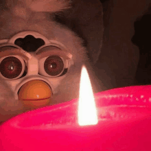 a furby doll is sitting next to a pink candle