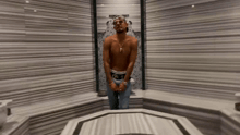 a man without a shirt is standing in a room with a striped wall .