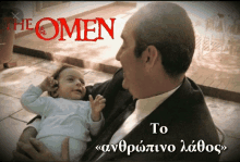 a man in a suit is holding a baby with the omen in red letters