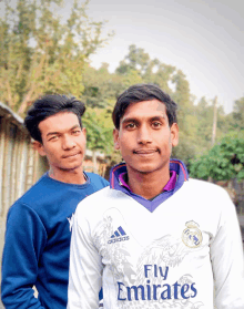 a man wearing a white fly emirates shirt stands next to another man