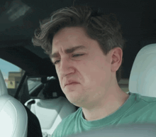 a man in a green shirt is sitting in the back seat of a car with his eyes closed .