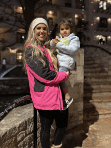 a woman in a pink jacket is holding a little girl in her arms