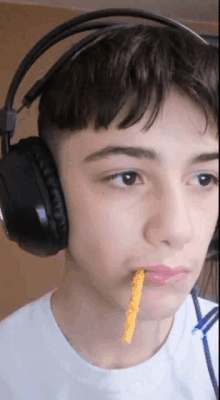 a young boy wearing headphones and holding a cheese stick in his mouth