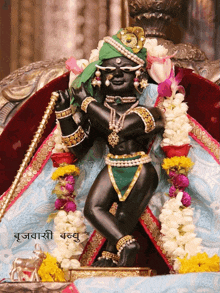 a black statue of a deity with a green turban is surrounded by garlands of flowers