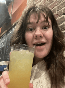 a woman drinking from a glass with a straw in front of a chalkboard that says " beer "