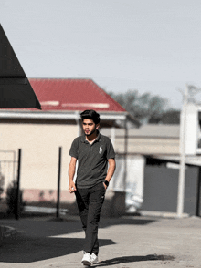 a young man wearing a black polo shirt and black pants walks down a street