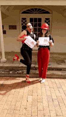 two women wearing red pants and red heels holding a sign that says ' i love you ' on it