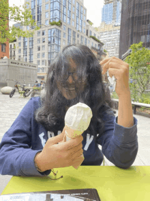 a woman sitting at a table eating an ice cream cone and wearing a blue sweatshirt with the letter y on the front