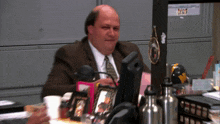 a man in a suit and tie sits at a desk with a bottle of water and a picture frame