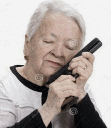 an elderly woman is holding a gun to her face with her eyes closed