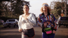two women are running down a street with one wearing a shirt that says just cal
