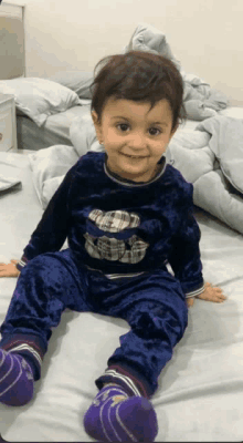 a little boy wearing a blue shirt with a bear on it is sitting on a bed