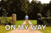 a man is walking down a dirt road with the words `` on my way '' written on the ground .