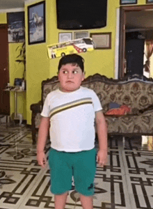 a boy in a white shirt and green shorts stands in front of a yellow couch