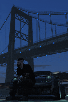 a man sits on the hood of his car under a bridge