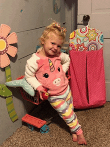 a little girl wearing a pink unicorn shirt is sitting on a shopping cart