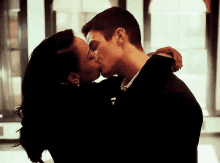 a man and a woman are kissing in a room in front of a window .