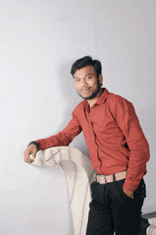 a man in a red shirt and black pants leans against a wall