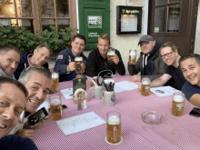 a group of men are sitting at a table holding beer mugs in front of a sign that says apfelwein bier