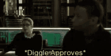 a man and a woman are sitting in front of a computer screen . the man is saying `` diggle approves '' .