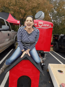 a woman is sitting on the roof of a dog house in front of a trailer that says racing style