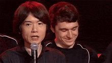 a man is speaking into a microphone while another man looks on in the background .