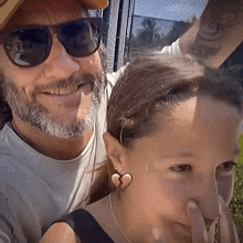 a man with a beard and sunglasses stands next to a little girl with a heart shaped earring