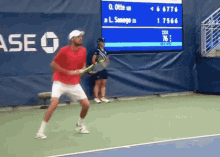 a man in a red shirt is holding a tennis racquet on a tennis court in front of a scoreboard that says ase